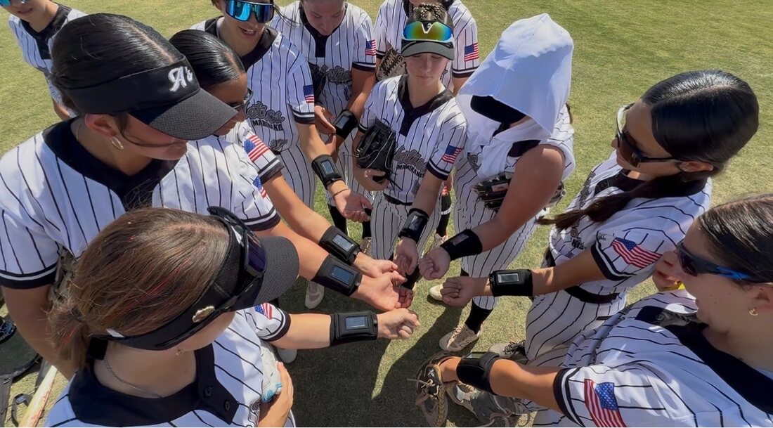 Fastpitch team huddle with DigiWrist armbands on their wrists